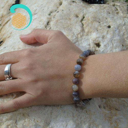 Bracelet en agate de Botswana au poignet d'une main de femme posée sur un rocher. daariayoga.com