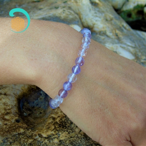 Bracelet d'amethyste au poignet d'une main au dessus d'un rocher. daariayoga.com